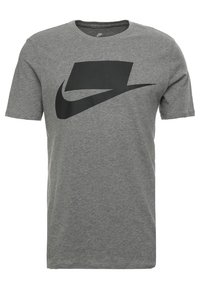 Šedé bavlněné tričko s černým logem Nike a designem složeným z klouzavého symbolu na přední straně. Krátké rukávy a kulatý výstřih.