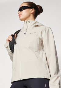 Hellbeige wasserdichte Jacke mit hohem Kragen, Reißverschluss und Reißverschlusstaschen. Verfügt über einen strukturierten Stoff und Logodetail am Ärmel.