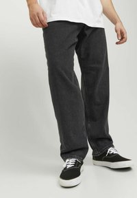 Jeans de mezclilla negros con corte holgado, que presentan una superficie texturizada y un diseño estándar de cinco bolsillos, combinados con zapatillas negras y cordones blancos.