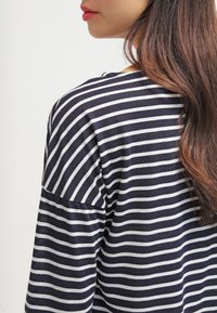 Námořnické a bílé pruhované tričko s dlouhým rukávem a volným střihem. Měkká textilie a design s nízko posazenými rameny zvýrazňují ležérní styl a pohodlí.
