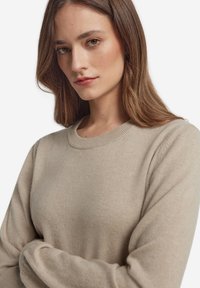 Beżowy sweter wełniany z okrągłym dekoltem, długimi rękawami, miękką fakturą i ściągaczami na mankietach. Minimalistyczny design bez wzorów i ozdób.