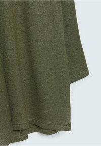 Oliivivihreä neulottu kangas, jossa näkyvät saumat ja pehmeä rakenne, esittää reunaa ja osaa hihasta vaaleaa taustaa vasten.