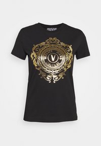 Musta puuvillainen t-paita, jossa on suuri kultainen koristeellinen emblem, jossa on ympyrän muotoinen design ja keskellä teksti "VERSACE JEANS COUTURE".