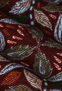 Cotton fabric with a textured ribbed surface featuring a leaf pattern in dark red, blue, green, and orange colors.