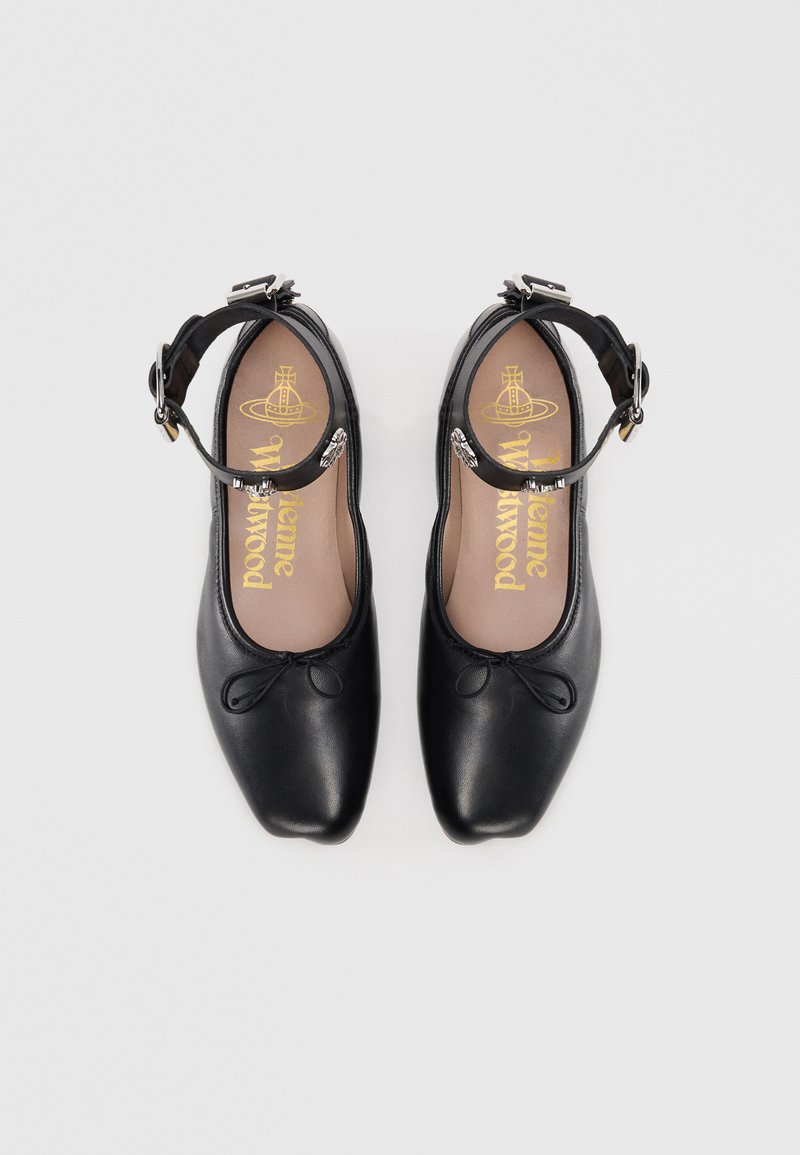 Ballerines en cuir noir avec un bout arrondi, une bride autour de la cheville et un nœud décoratif. L'intérieur présente un rembourrage marron avec des détails du logo en or.