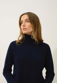 Granatowy sweter z golfem wykonany z dzianiny, z prążkowaną fakturą i wertykalnymi szwami, z długimi rękawami i luźnym krojem.