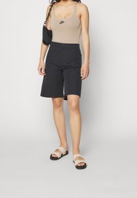 Beige linne med svart Nike-logga, kombinerat med svarta shorts och beiga sandaler med vridna remmar. Enkelt, avslappnat design totalt sett.