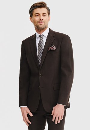 Ciemnobrązowy garnitur z dwoma guzikami, klapkami i bocznymi kieszeniami. Biała koszula i wzorzysty krawat, poszetka z kwiatowymi akcentami.