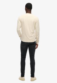 Chemise à manches longues de couleur crème en tissu doux, associée à un jean foncé. Présente un col rond et un design minimaliste.