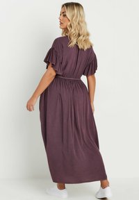 Maxiklänning i mauve-tyg med korta volangärmar, samlat midja och svävande silhuett. Stylar med vita sneakers.