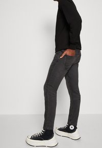 Jean gris à coupe slim, tissu en denim de poids moyen, et design classique à cinq poches. Associé à des baskets montantes noires et une chemise noire.