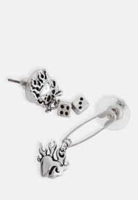 Silver stud earrings with flame and heart designs, featuring dice accents. Detailed textures and polished finish enhance visual interest.