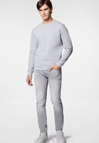 Jasnoszara bluza z okrągłym dekoltem i długimi rękawami, w połączeniu z jasnoszarymi dżinsami slim fit i białymi sneakersami. Prosty, casualowy design.