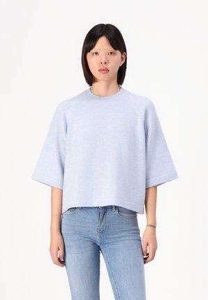 Lyseblå strikket genser med korte, brede ermer og rund hals. Myk tekstur og avslappet passform, kombinert med tettsittende blå jeans.