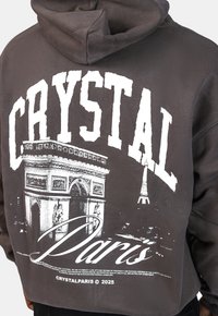 Šedá mikina s kapucí se bílou grafikou oblouku vítězství a Eiffelovy věže, s nápisem "CRYSTAL" v tučném písmu nahoře.