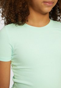 Maglietta a maniche corte verde menta a costine con scollatura rotonda, che presenta un design aderente e una texture morbida.