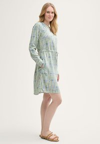 Langärmliges Kleid im hellgrünen und blauen Karomuster, mit tailliertem Design, Taschen und einem Kragen. Kombiniert mit beigen Sandalen.