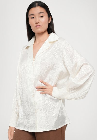 Cămașă albă cu nasturi, cu un design texturat și semi-transparent, având guler și manșete elastice. Material neted cu modele subtile.