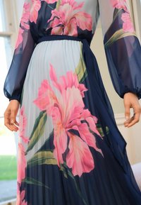 Maxikleid mit Blumenmotiven aus durchscheinendem marineblauem Stoff, großen rosa Blumen, entspanntem, tailliertem Bund und langen Puffärmeln mit gefaltetem Design.