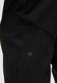 Crne atletične hlače izrađene od teksturirane tkanine s uzorkom u obliku saća; uključuju mali logo na donjem dijelu noge.