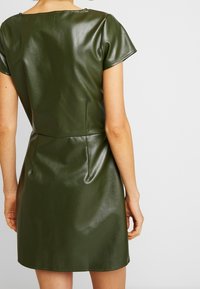Olivenfarbendes Kunstlederkleid, kurze Ärmel, Rückennahtdetails, glatte Textur, tailliert und mit leicht ausgestellter Silhouette.
