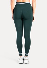 Mörkgröna leggings med texturerad yta, hög midjeresår med randigt mönster, tillsammans med vita träningsskor.