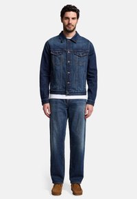 Giacca di denim blu con chiusura a bottoni, due tasche sul petto e colletto; abbinata a jeans azzurri e scarpe mocassino marroni.