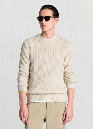 Maglione beige lavorato a maglia con motivo a costine verticali, scollo rotondo e polsini a costine. Abbinato a una maglietta bianca e pantaloni khaki chiaro.