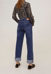 Jeans z wysokim stanem, prostymi nogawkami w ciemnym denimu z podwiniętymi mankietami, zestawione z czarną i jasnobrązową w paski bluzką. Widoczne są dwie tylne kieszenie.