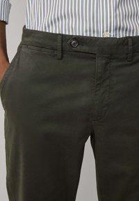 Pantaloni verde scuro realizzati in tessuto morbido, con chiusura a bottone, tasche laterali e dettagli di cucitura sottile.