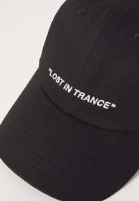 Μαύρο καπέλο μπέιζμπολ από βαμβακερό τουίλ με λευκή κεντημένη επιγραφή "ΧΑΜΕΝΟΣ ΣΤΟ ΤΡΑΝΣ". Διαθέτει καμπυλωτό γείσο και σχέδιο έξι πάνελ.