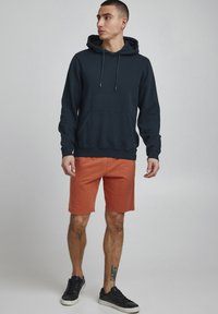 Jūras spēku kapuce ar regulējamu šņorīti, priekšējais kabata; kopā ar oranžām šortiem un melniem sporta apaviem. Gluda auduma, brīvs piegriezums.