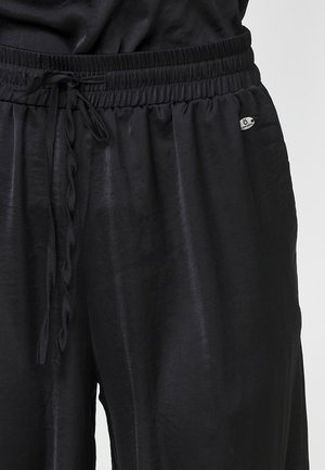Pantalons légers noirs avec une taille élastique, un cordon de serrage et un patch logo. Texture lisse et coupe décontractée.