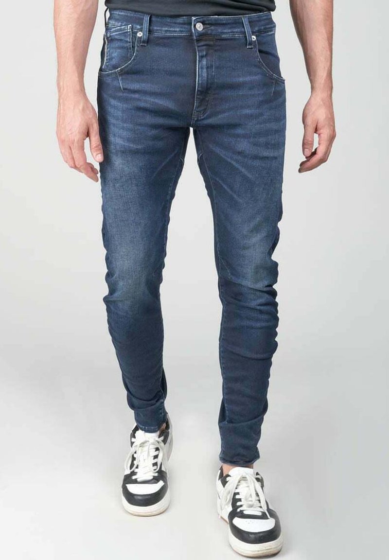 Jeans oscuros de corte ajustado con diseño de cinco bolsillos, fabricados en denim. Combinados con zapatillas negras y blancas. Textura suave, con un desvanecimiento mínimo.