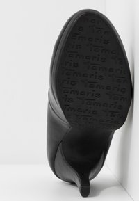 Chaussure noire en cuir à talon haut avec un bout pointu et une texture fine. La semelle présente un marquage en relief et un talon aiguille élancé.