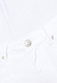 Gros plan sur une ceinture en denim blanc avec un bouton argenté et des passants de ceinture, mettant en valeur la texture du tissu et les détails de couture.