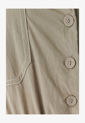 Beige-kangastooted, millel on silmapaistev tasku kontrastsete valgete õmblustega ja neli suurt ümmargust nööpi külgedel.