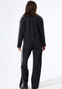 Zwarte sweatshirt en broek van een zachte, gestructureerde stof met witte zijstrepen. Het ontwerp heeft een ontspannen pasvorm en lange mouwen.