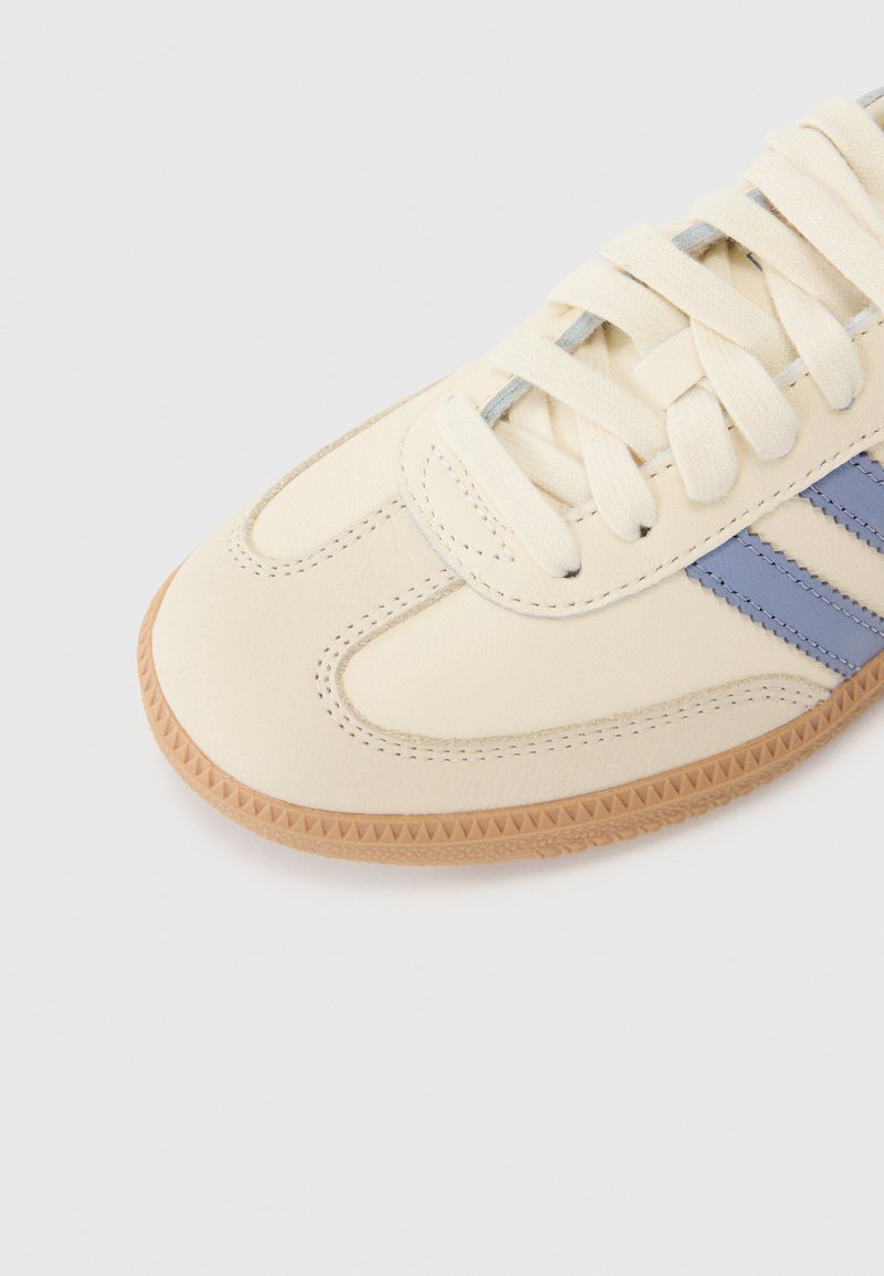 Cremfarbene Sneaker mit hellblauen Streifen, aus glattem Leder gefertigt. Verfügt über eine strukturierte Gummisohle und flache Baumwollschnürsenkel.