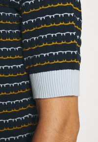 Stickad tröja med horisontella ränder i marinblått, vitt och senapsgult, med en ribbad ljusblå mudd och ett texturerat mönster.