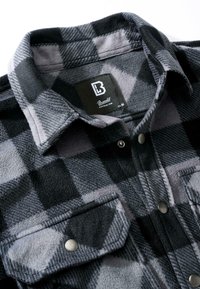 Čierna a sivá kockovaná flanelová košeľa s klasickým golierom, zapínanými vreckami na gombíky a jemnou textúrou, s výraznou štítkovou značkou vo vnútri.