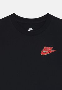 Čierne tričko s okrúhlym výstrihom, ktoré má na ľavej strane hrude červené a zelené logo Nike. Tkanina vyzerá hladko a neformálne.
