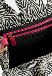 Černobílá vzorovaná ta�ška přes rameno s růžovým zipem a podšívkou, se strukturovaným tvarem a textilním materiálem. Uvnitř obsahuje branding.