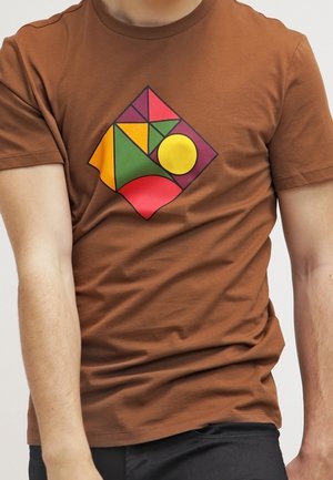 Camiseta marrón con un patrón geométrico colorido que incluye un círculo amarillo, formas rojas, verdes y moradas centradas en el pecho.