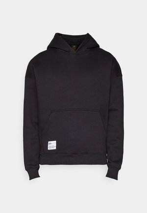 Czarna bluza z kapturem z dużą kieszenią kangurka z przodu oraz małą, białą, prostokątną metką po lewej stronie u dołu.