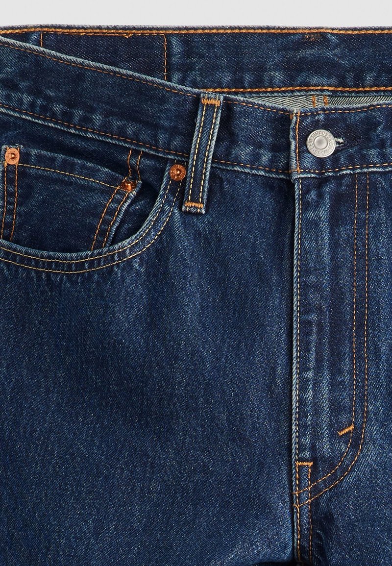 Dunkelblaue Jeans aus Denim mit orangefarbener Steppnaht, Knopfverschluss und Standardtaschen. Der Stoff zeigt eine leichte Textur und ein klassisches Design.