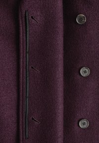 Wollmischungsmantel in tiefem Lila mit strukturiertem Finish, ausgestattet mit einem einzigen Knopfverschluss, zwei seitlichen Taschen und schwarzen genähten Details.