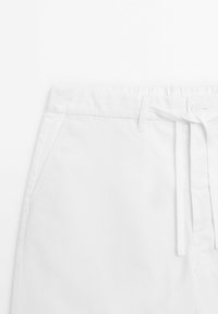 Hvide bomuldsshorts med elastisk talje, snørelukning og sidelommer. Glat tekstur og simpelt design uden synlige mønstre.