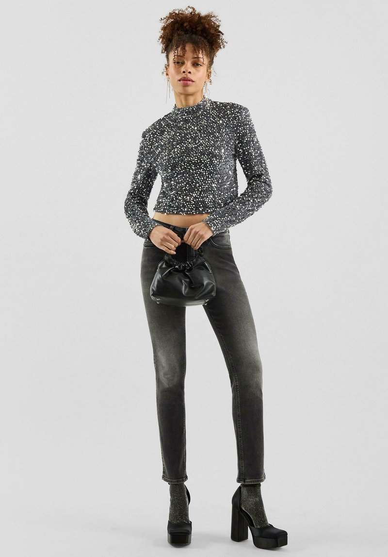 Szary, dopasowany, cekinowy top na krótko z wysokim kołnierzem; w parze z ciemnoszarymi dżinsami i masywnymi czarnymi platformowymi szpilkami. W ręku czarna torebka kopertówka.