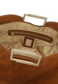 Interno della borsa in suede marrone con una fodera beige, dotato di una tasca con zip, una patch con logo e un dettaglio in metallo dorato sulla maniglia.